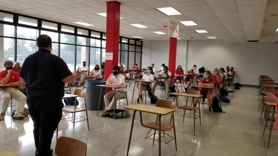 Fr. Mark Cavara speaks to students in the cafeteria, where desks have replaced tables so social distancing can be enforced.